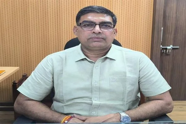 हल्के रंग की शर्ट और चश्मा पहने एक अधिकारी कार्यालय में कुर्सी पर मेज के पीछे बैठे हुए
