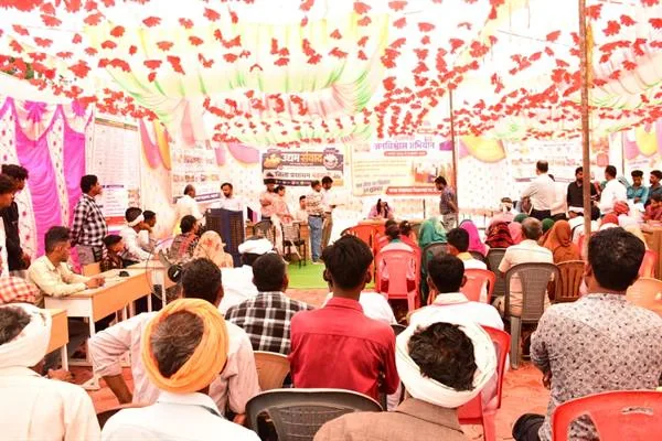 सजे हुए पंडाल में कुर्सियों पर बैठे ग्रामीण और सामने मेजों पर आवेदन लेते कर्मचारी