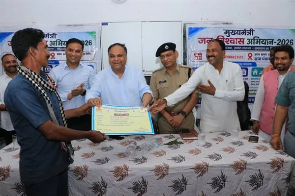 एक हितग्राही को प्रमाणपत्र सौंपते अधिकारी और जनप्रतिनिधि, पीछे पुलिस अधिकारी व अन्य लोग खड़े हैं