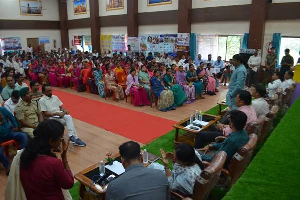 सभागार में कुर्सियों पर बैठे ग्रामीणों, महिलाओं, अधिकारियों और जनप्रतिनिधियों के बीच संवाद करते लोग