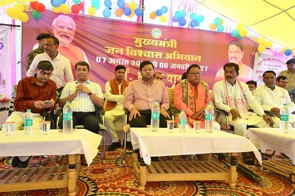 मंच पर कुर्सियों पर बैठे विधायक, प्रशासनिक अधिकारी और अन्य लोग, सामने मेजों पर पानी की बोतलें तथा पीछे जन-विश्वास अभियान का बैनर