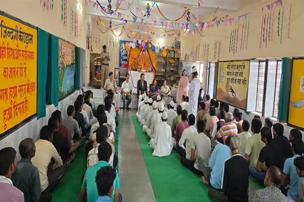 सजाए गए जेल सभागार में अधिकारी मंच के पास बैठे हैं और फर्श पर कतारों में लोग कार्यक्रम सुन रहे हैं
